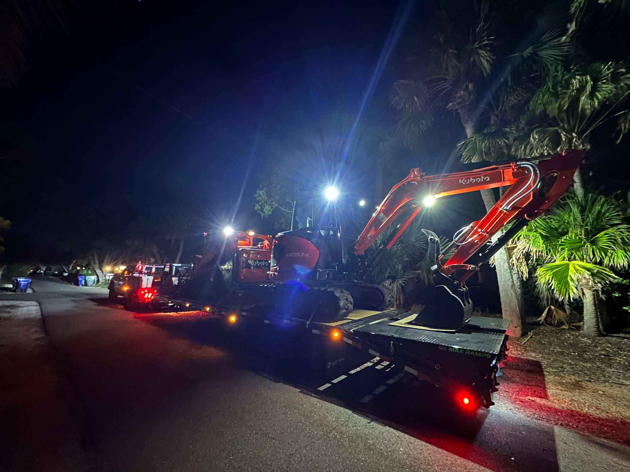 Emergency services with back hoe and skid steer on a trailer at night.